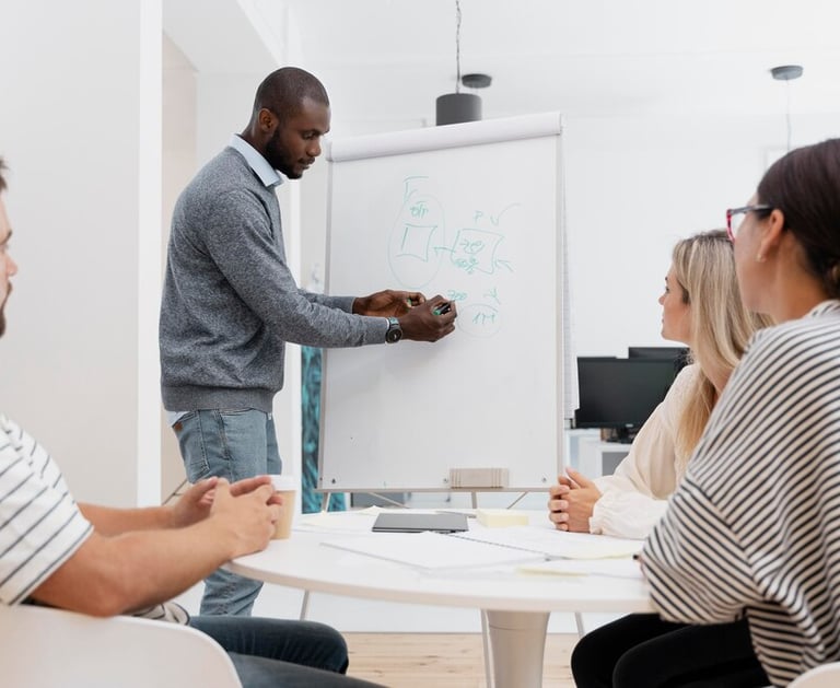 Un homme présente à un groupe lors d'une réunion devant un tableau blanc.