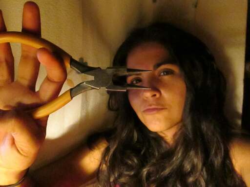 En una habitación con poca luz, una mujer sostiene un par de alicates amarillos de punta larga 