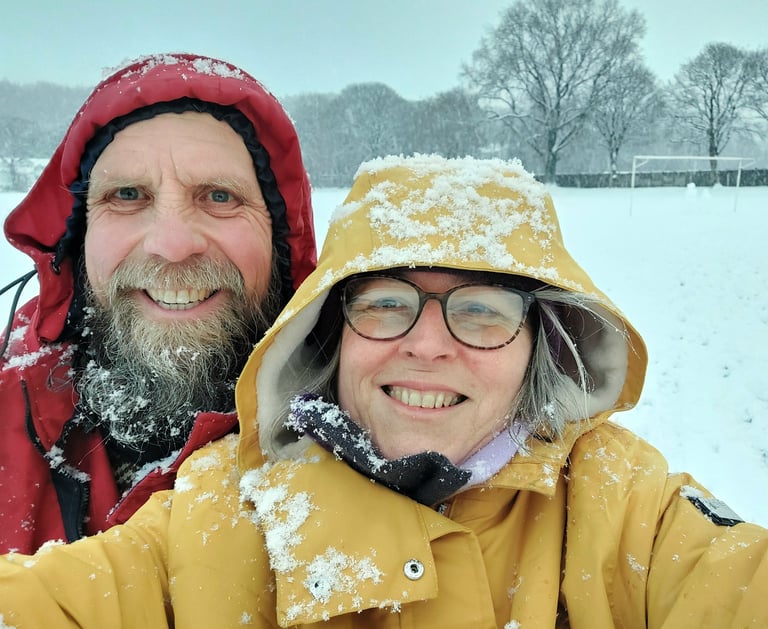 A man with a beard in a red coat and a woman with glasses in a yellow coat in the snow