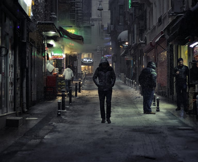 Pessoa de casaco andando em um beco à noite, em bairro humilde, transmitindo solidão e introspecção.