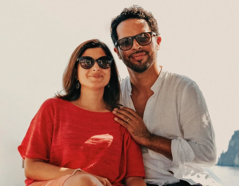 Due persone sedute all’aperto che sorridono, indossando occhiali da sole.