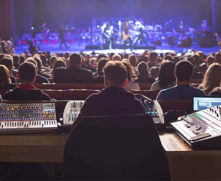 Live event technician operating multiple audio mixers during a stage performance, representing Sonus' technical support servi