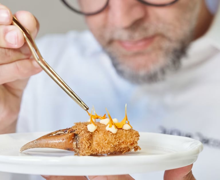 Chef Quique Dacosta garnishing crab claw with edible flowers using tweezers.
