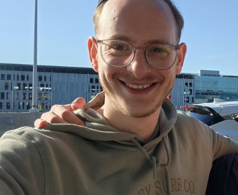Smiling man with glasses and a yarmulke wearing a tan Hurley hoodie outdoors on a sunny day.