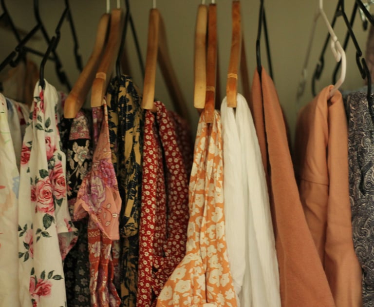 vestidos florales y prendas estampadas colgadas en ganchos de madera y plástico dentro de un clóset.