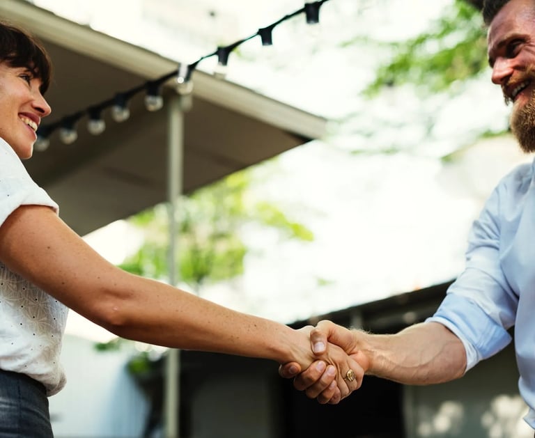 Smiling business professionals shaking hands outdoors to celebrate a successful partnership agreement.