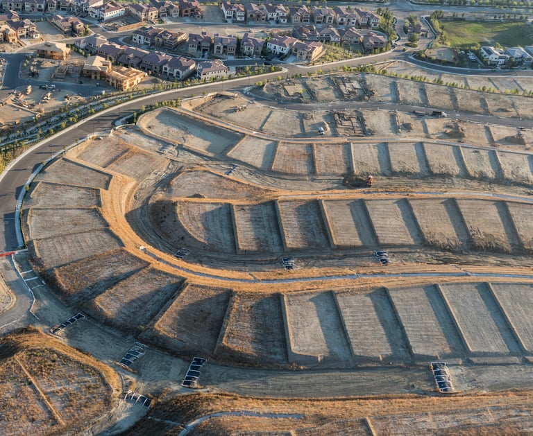 Aerial view of new housing development construction site with terraced land lots and suburban infrastructure.
