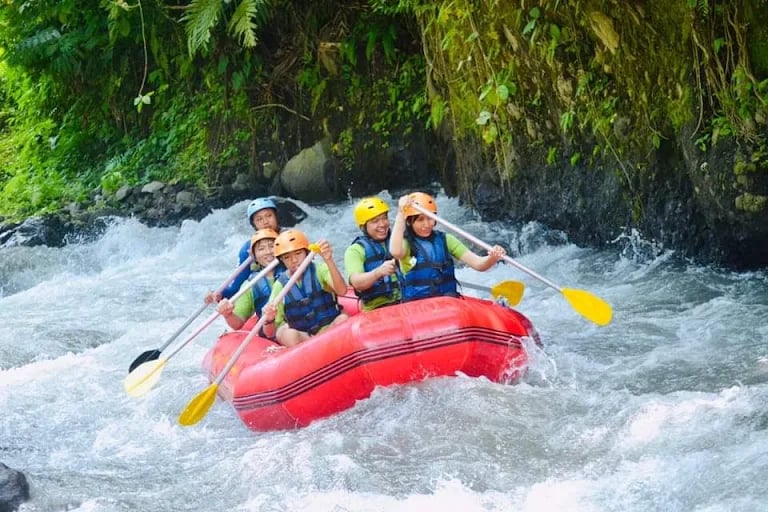 Group of tourists in life jackets white water rafting on a red raft through river rapids.