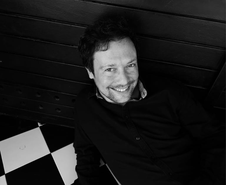 A smiling man with a beard wearing a black shirt in a black and white portrait.