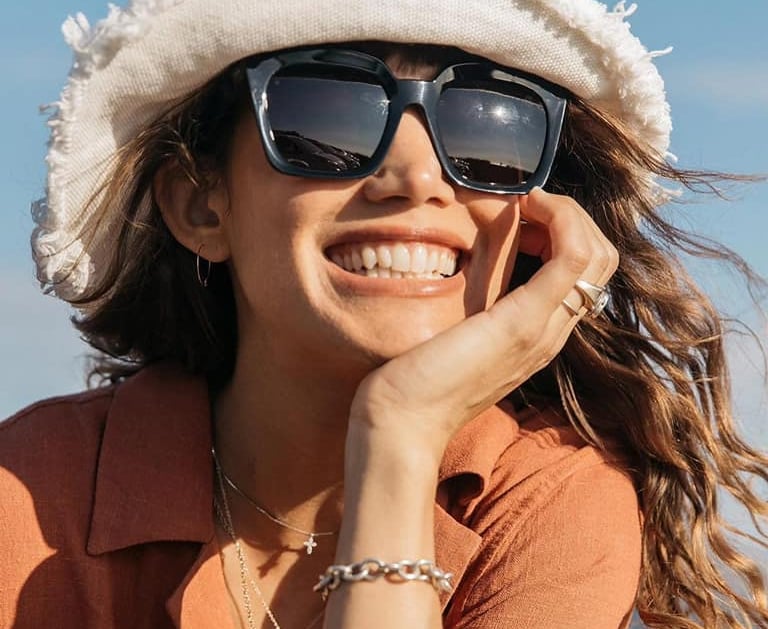 Woman smiling with designer sunglasses, available at Edge Optics