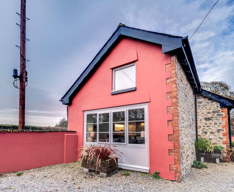 A charming pink rendered cottage with stone walls and large windows in a rural setting.
