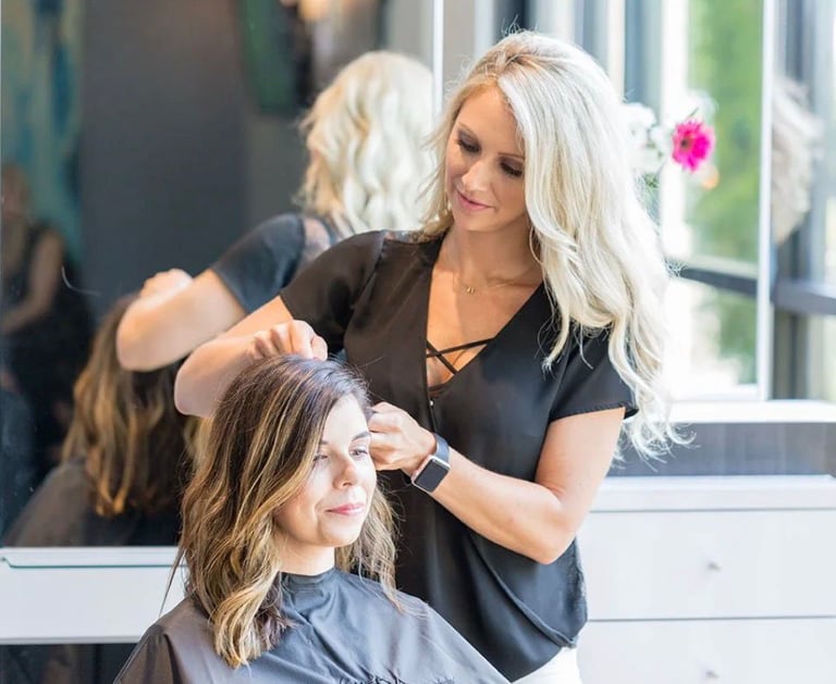 Professional blonde hair stylist styling a client's brunette hair at a modern hair salon.