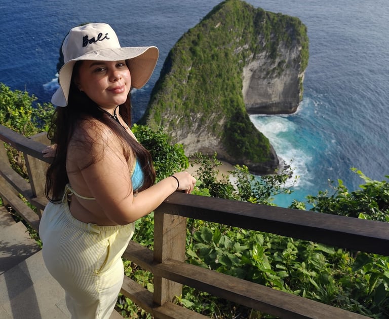 A woman in a Bali sun hat overlooking the scenic Kelingking Beach cliffs in Nusa Penida.