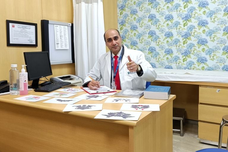 Dr. Prabal Frank Nandwani in OPD giving thumbs up, with Rorschach inkblot test cards & DSM-5 manual
