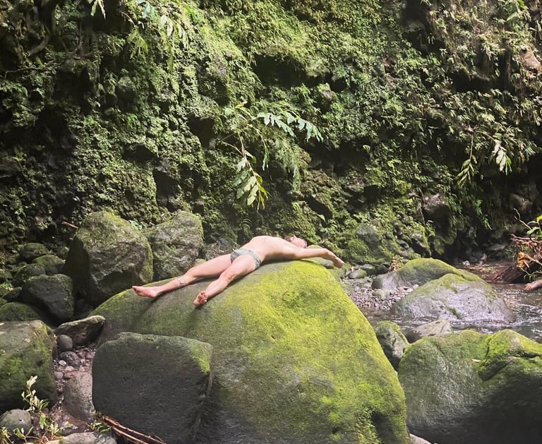 man laying on the rocks under a waterfall after a hike