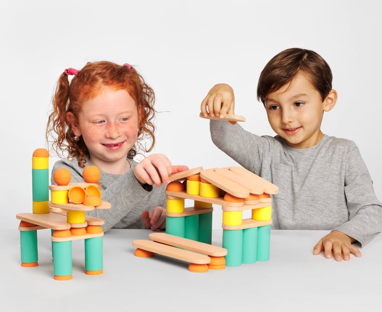 Two children creating two structures from colorful silicone and wooden figures
