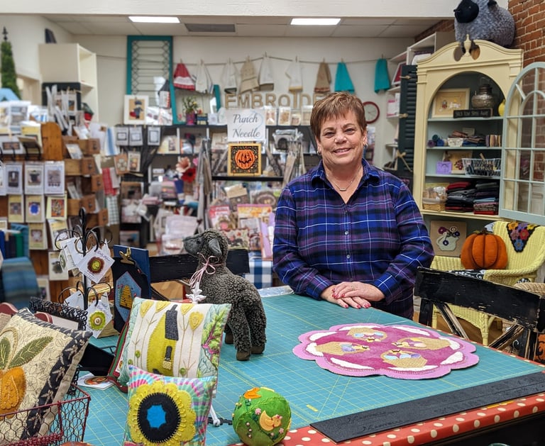 Shop owner, Cheryl, stands in front of the pattern table in The Black Sheep Wool Shop