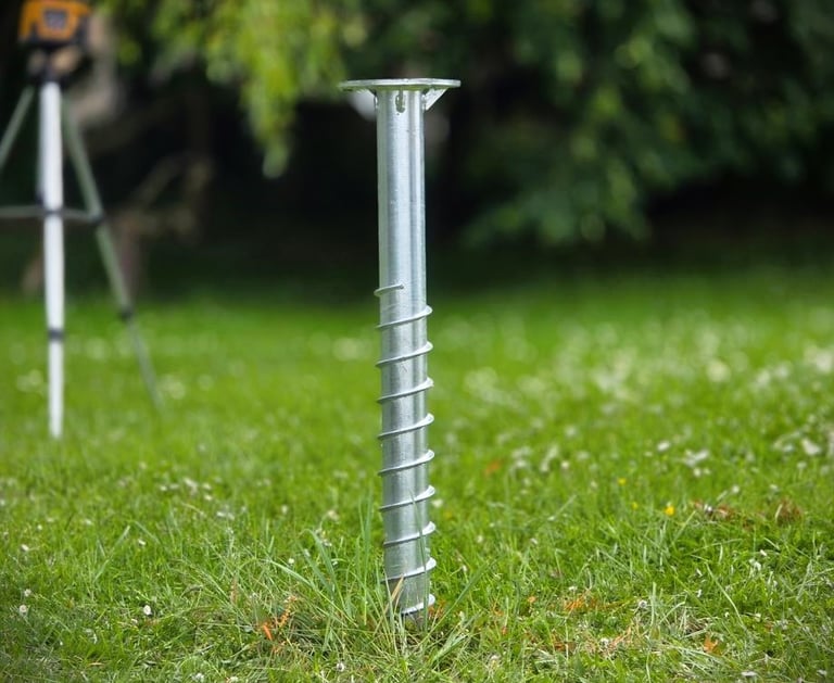 Galvanized steel ground screw anchor installed in a green lawn for deck and shed foundations.