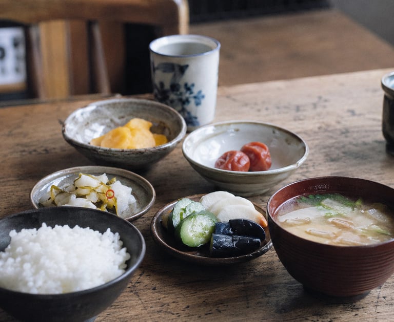 Traditional Japanese breakfast with steamed white rice, miso soup, pickled vegetables, and umeboshi.