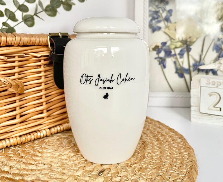 Glossy white ceramic urn with soft curves, black script engraving “Otis Josiah Cohen 25.09.2024” and