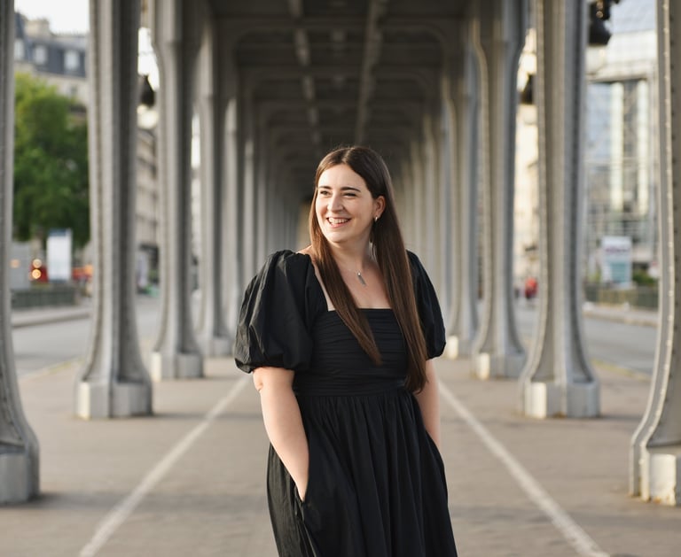Une femme sourit en regardant à droit, seule sur le pont de bir hakeim sous les rails du métro, il fait beau