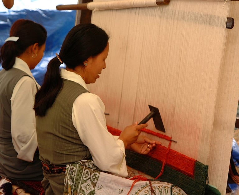 Two women weaving traditional red and green textiles on a large upright manual floor loom.