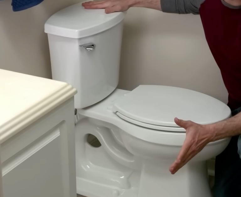 A man demonstrates a white dual-flush ceramic toilet installation in a bathroom.