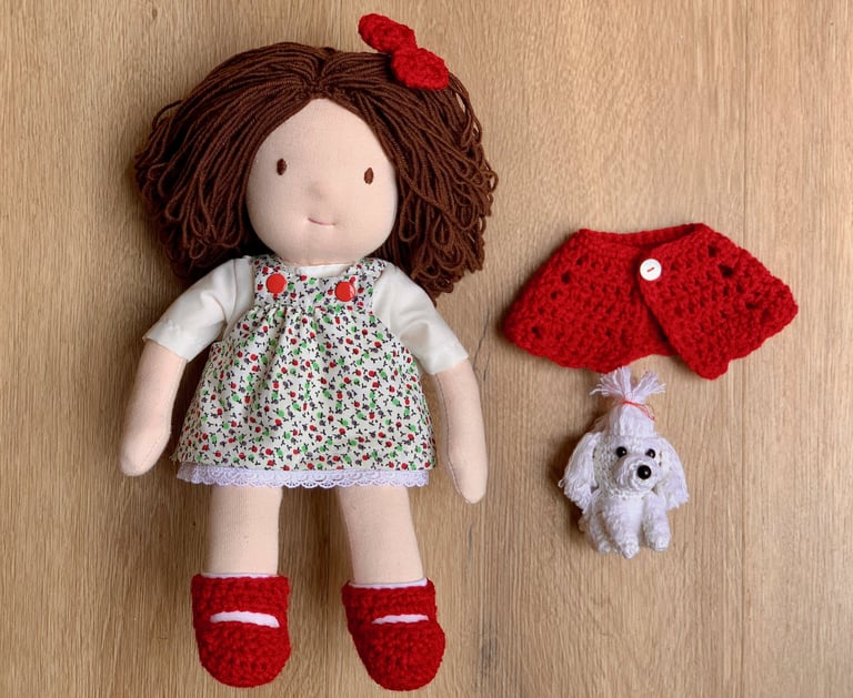 Muñeca Waldorf hecha a mano con cabello castaño, vestido floral, zapatos rojos y un pequeño perrito 