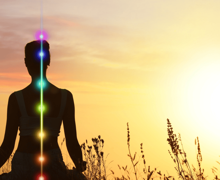 Silhouette of a woman practicing yoga at sunset with seven glowing chakra symbols aligned along her spine.