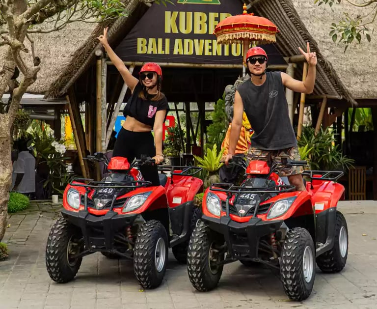 A couple poses on red ATVs for a Kuber Bali Adventure tour in a tropical jungle setting.