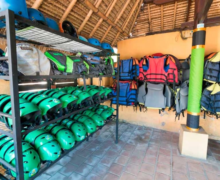 Rows of green safety helmets and life jackets for river rafting stored in an outdoor gear hut.