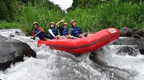 Excited group white water rafting in a red boat through river rapids with lush greenery.