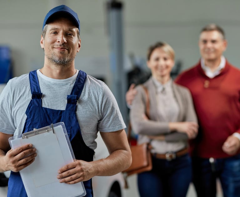 smiling handyman holding a clipboard in an Auckland workshop with clients behind him