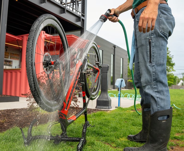 A bike flipped upside down, on the grass, with someone next to it spraying it with a hose