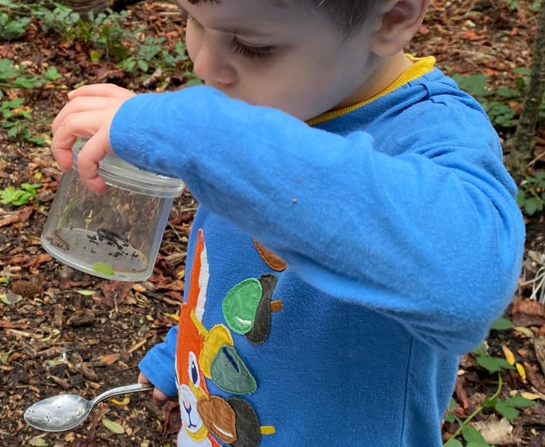 a young boy is holding a bug pot and spoon. He is looking at a bug in the pot.