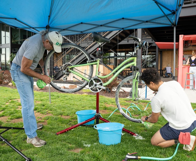 Two people cleaning a mounted bike with sponges