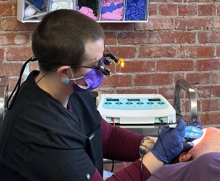 Sam, a skilled practitioner, with specialized eyewear on, treating a client with needle epilation