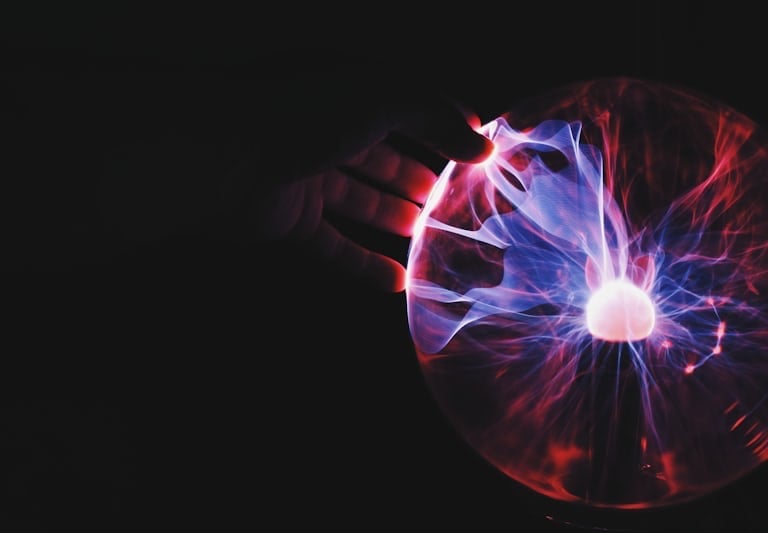 immagine di una mano che toccando una sfera illuminata questa si trasforma in raggi di corrente elet