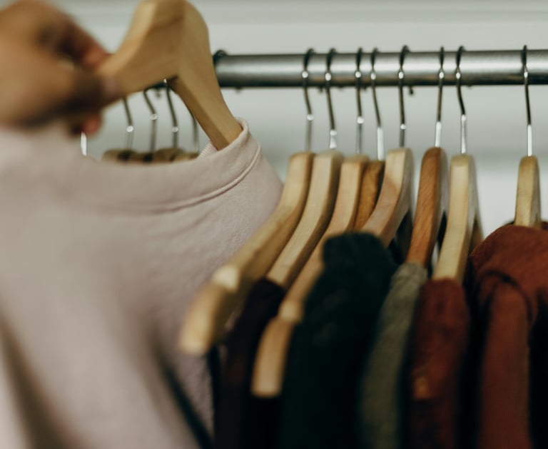 Una mano seleccionando un suéter rosa de un perchero con ganchos de madera para organizar el clóset.