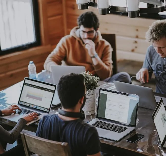 a group of people sitting around a table with laptops