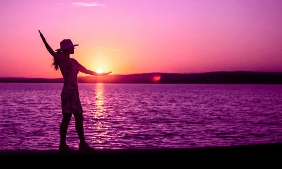 person practicing mindfulness for pain on a beach, using yoga or tai-chi. Purple sunset