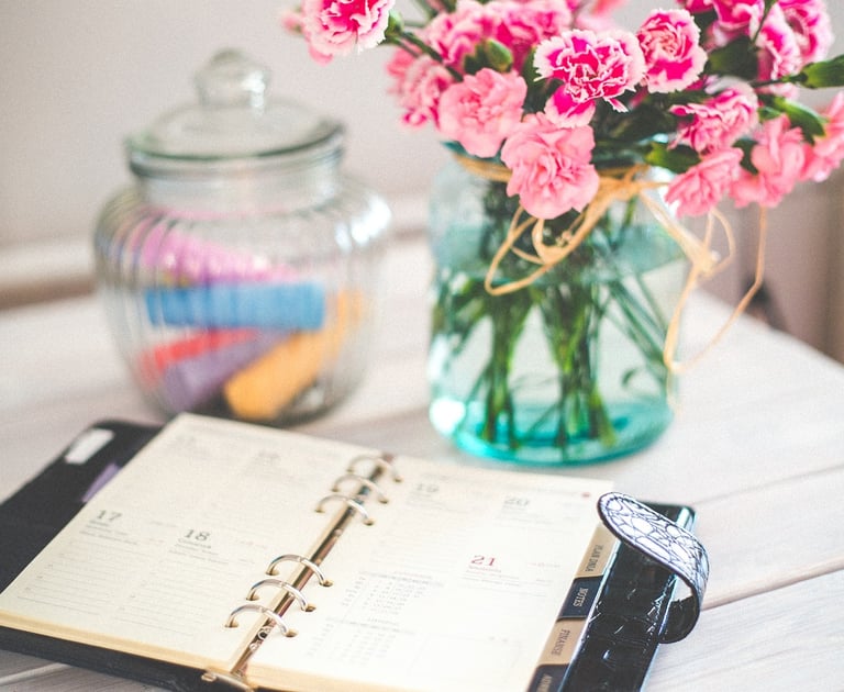 Agenda ouvert à côté d'un vase de fleurs fraîches, symbolisant une organisation soignée et la planification attentive des ses
