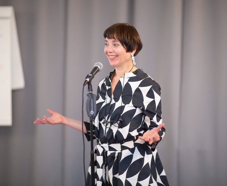 Female public speaking trainer behind microphone, energetic smiling while teaching.