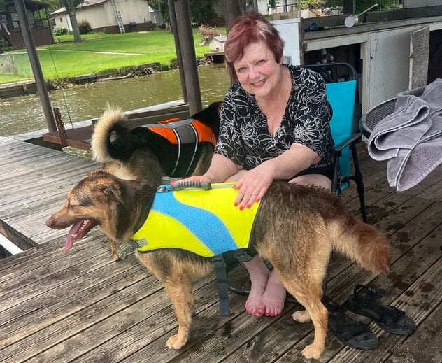 Photo of Debbie, seated on a lake dock, tending to two dogs wearing colorful life vests.