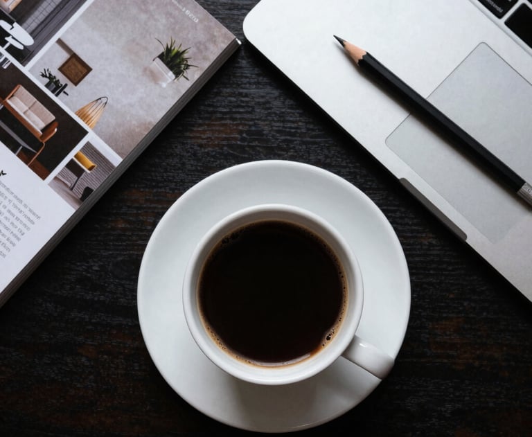 A top-down view of a designer's desk with a cup of coffee, architectural magazines, and a professional digital drafting pencil.