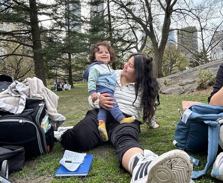 A mother holding her toddler while sitting on the grass in Central Park.