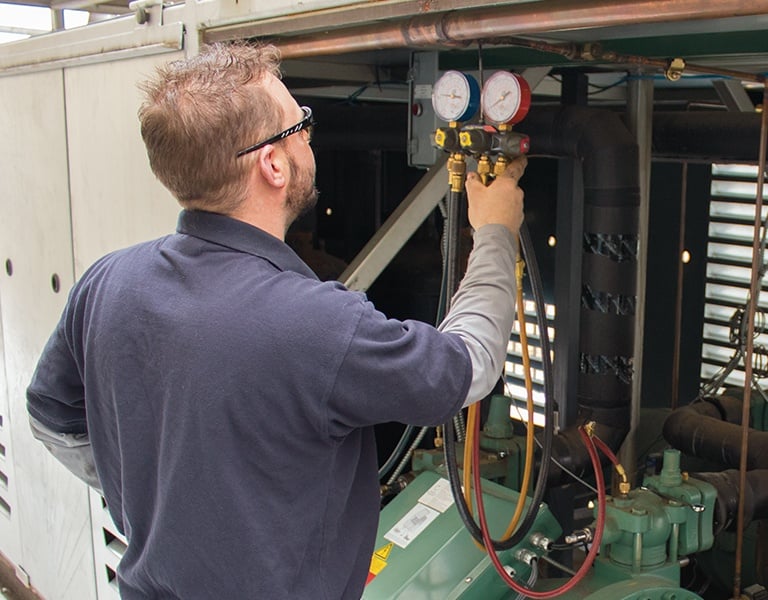 Professional HVAC technician using a manifold gauge set to check pressure on a commercial chiller unit.