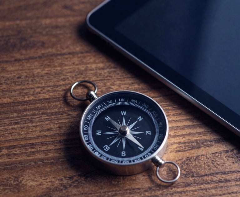 Minimalist photography of a compass and a tablet on a wooden desk. Deep navy blue shadows and warm light, symbolizing direction and strategy.