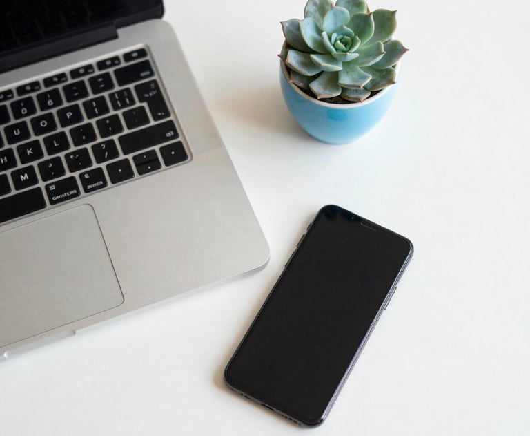 An overhead shot of a clean, minimalist desk with a silver laptop and a smartphone. A small cyan blue succulent pot adds a touch of life to the off-white surface.