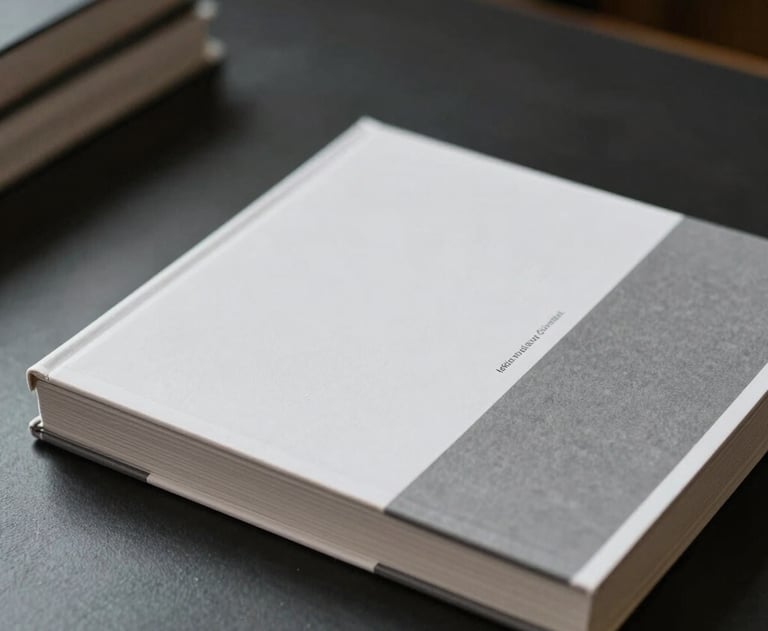 A stack of minimalist design books with white and gray covers on a dark desk. Soft shadows, International / General.